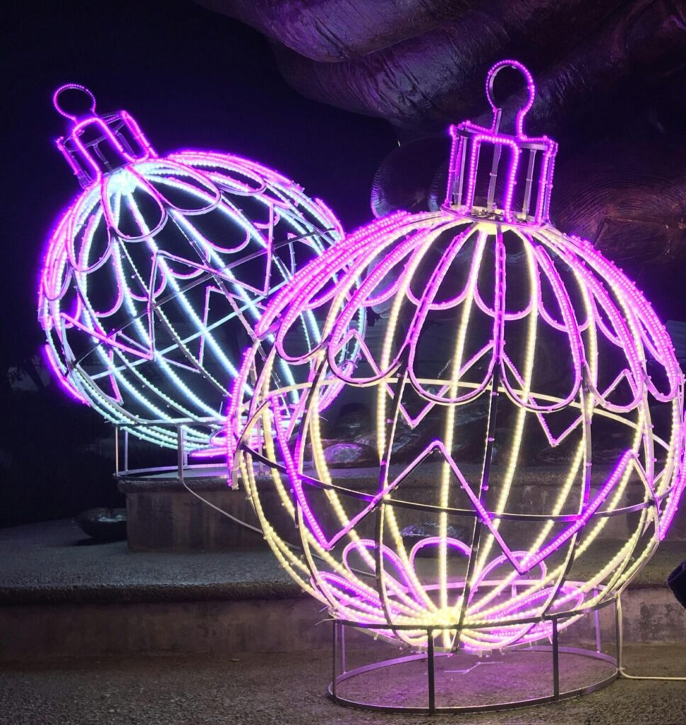 A young boy sitting with large, brightly lit Christmas decorations at night.